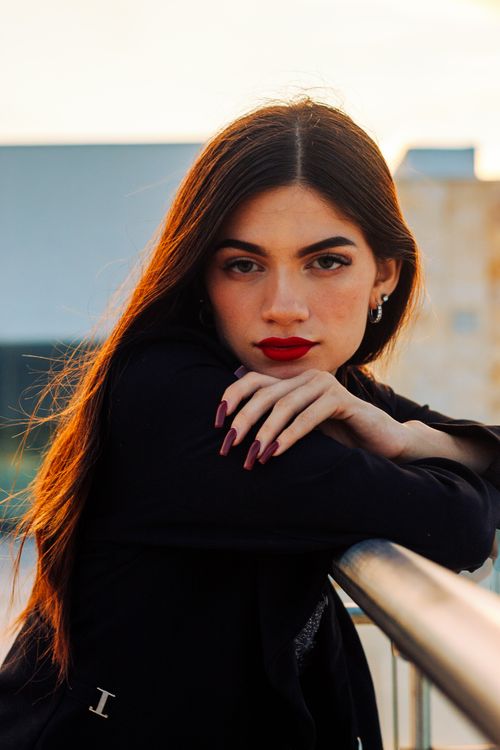 Free Stylish outdoor portrait of a young woman leaning on a railing, showcasing elegance and confidence. Stock Photo