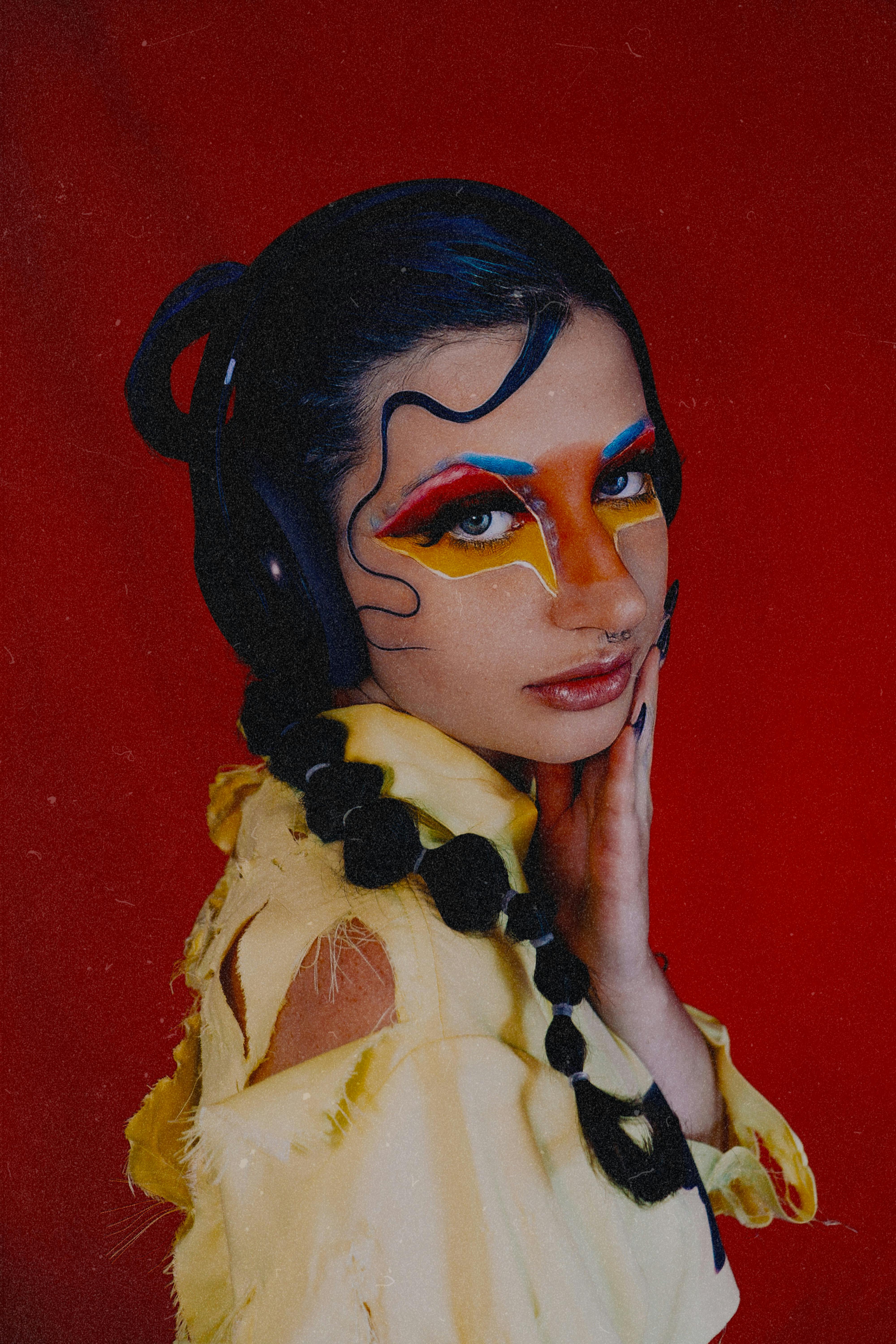 Artistic portrait of a woman with vivid makeup against a red background.