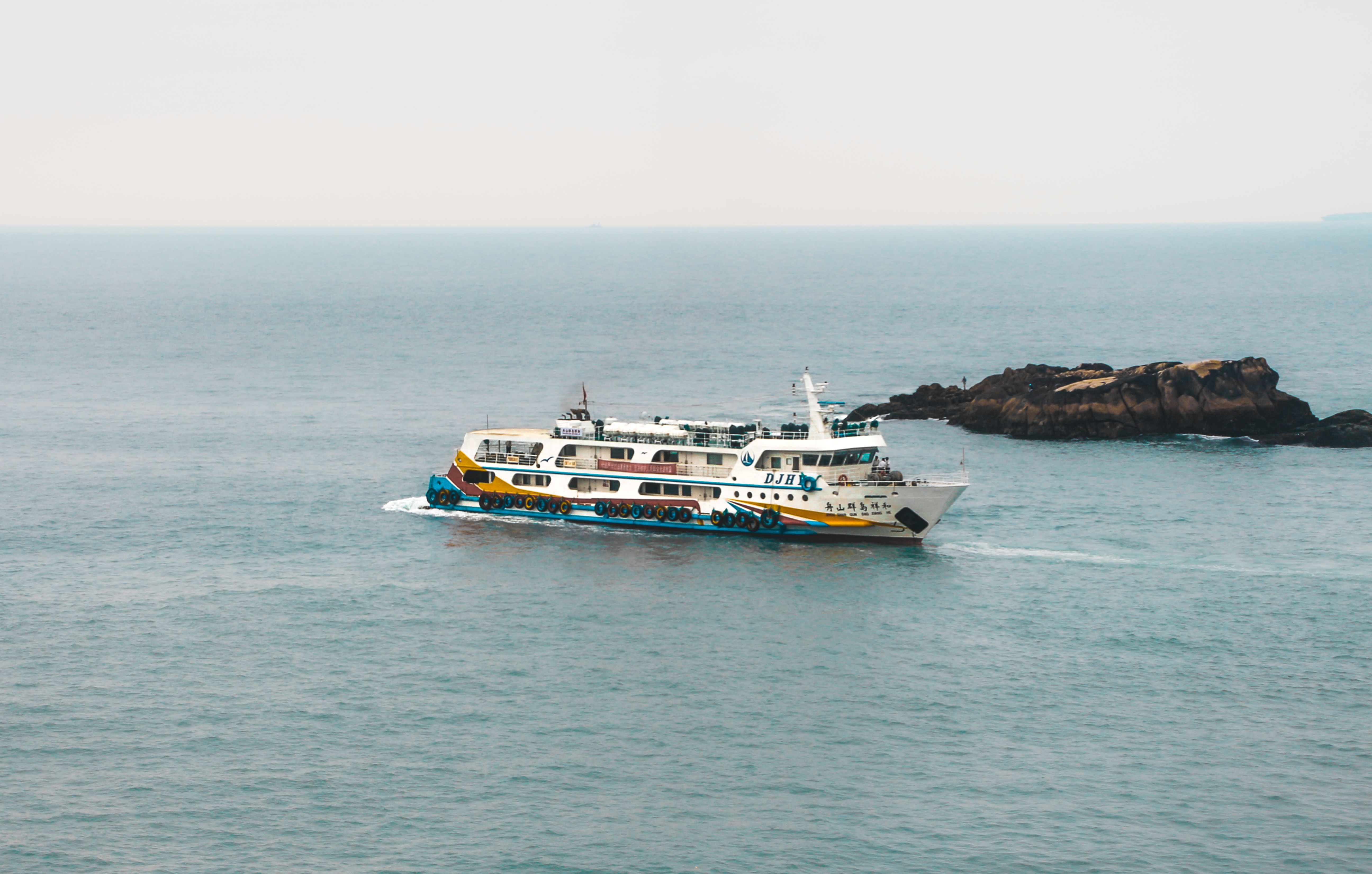 A colorful ferry cruising through serene coastal waters with distant rocky outcrops visible.