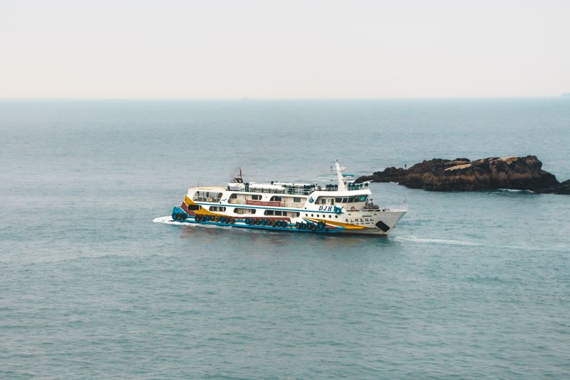A colorful ferry cruising through serene coastal waters with distant rocky outcrops visible.