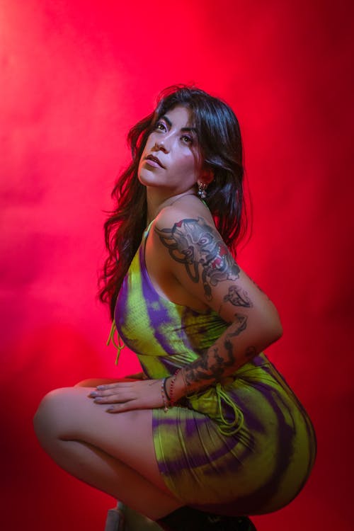 Young Woman with Tattoos Posing in a Dress against Red Background 