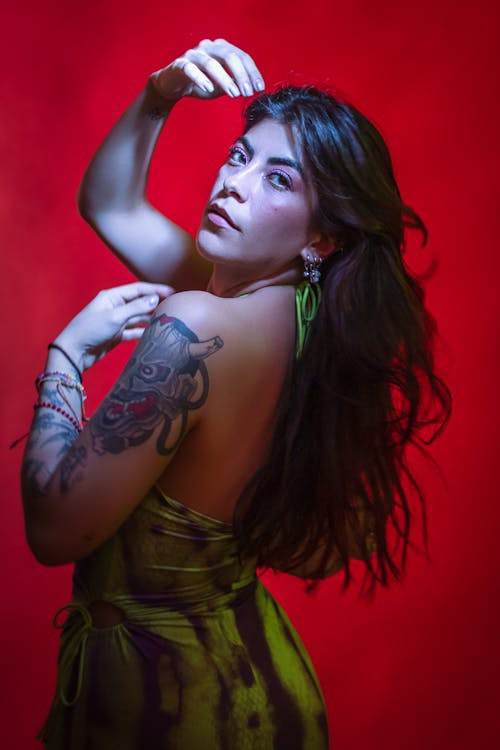 Young Woman with Tattoos Posing in a Dress against Red Background 