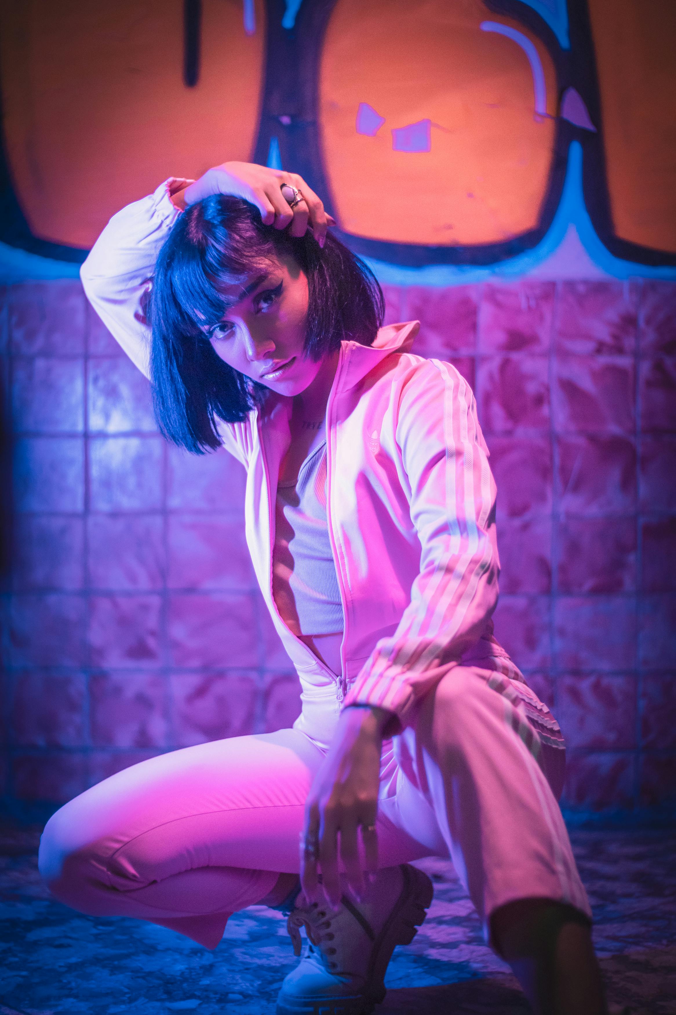 Young woman in a stylish tracksuit poses artistically against vibrant graffiti, embodying urban fashion.