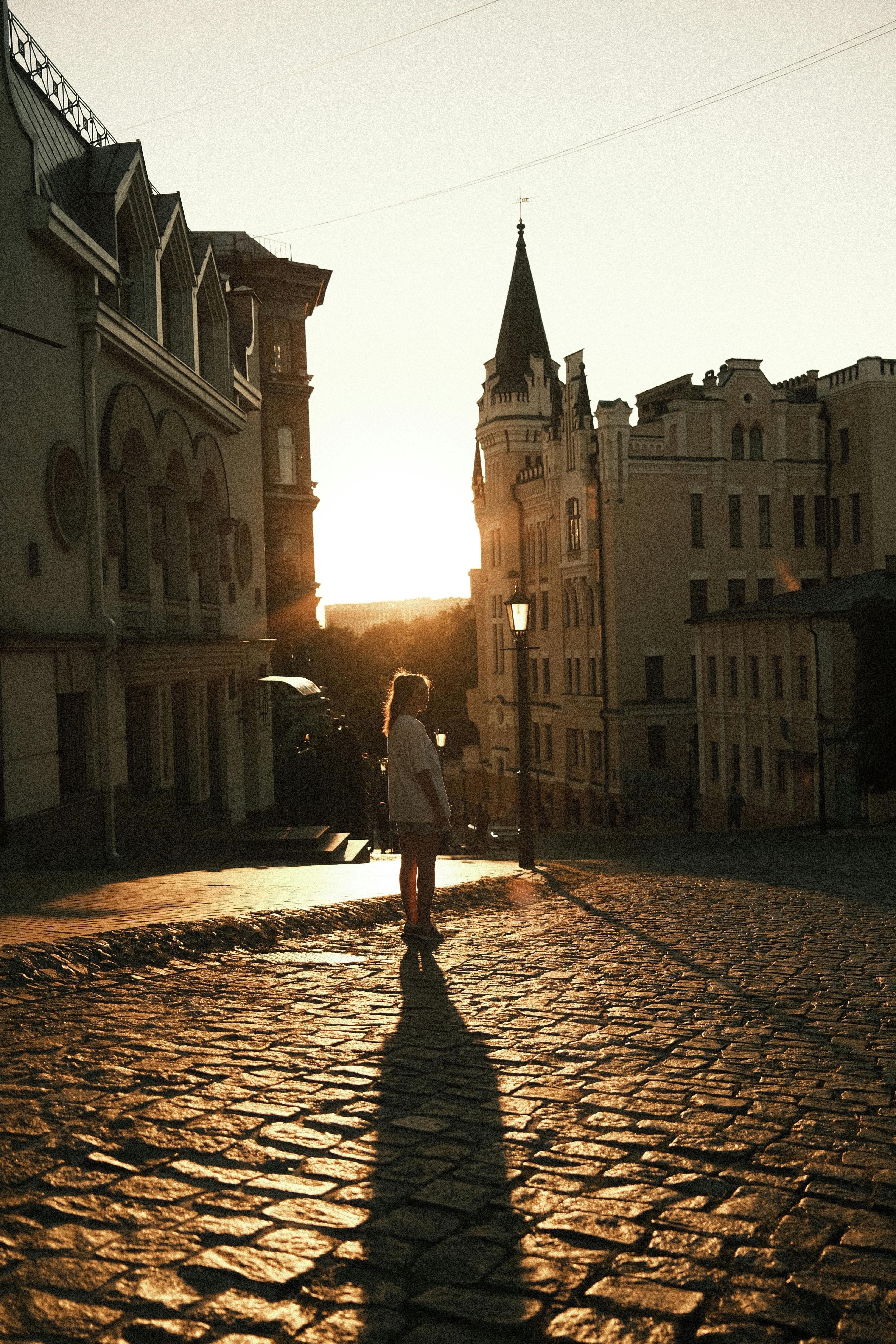 A woman walking through cobbled streets in Kyiv at sunset, creating a picturesque urban scene.