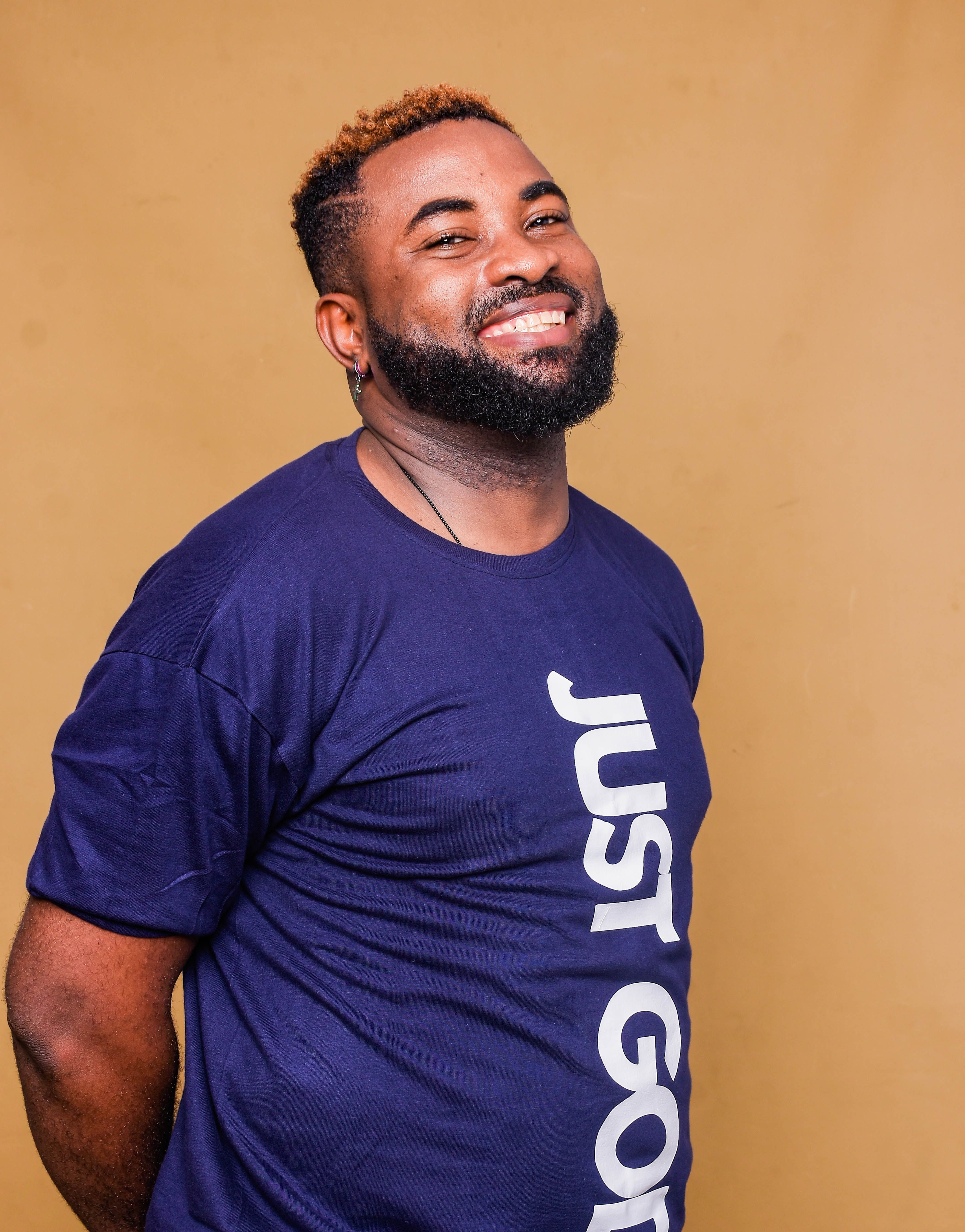 Portrait of a smiling African American man standing against a plain background, wearing a blue t-shirt.