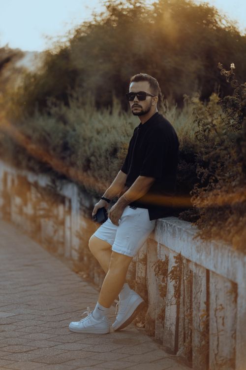 Free Fashionable man leans on a stone wall in an urban setting, basking in the sunset glow. Stock Photo