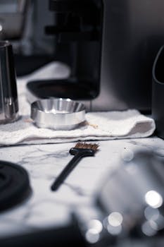 Detailed shot of coffee tools and brush on marble counter, with soft lighting.