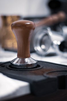 A detailed view of a wooden coffee tamper on a dark surface, essential for espresso preparation.