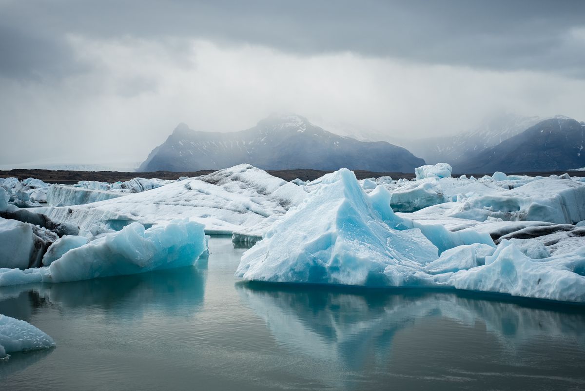 Icebergs drifting in a glacial lagoon below mountains — photo by Thibaut Tattevin on Pexels