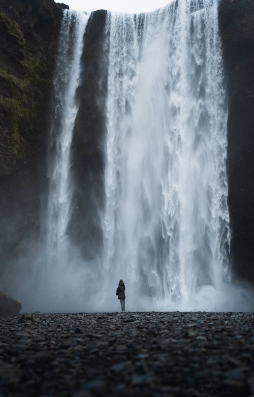 Free A breathtaking waterfall cascades majestically with a lone figure standing in awe. Stock Photo