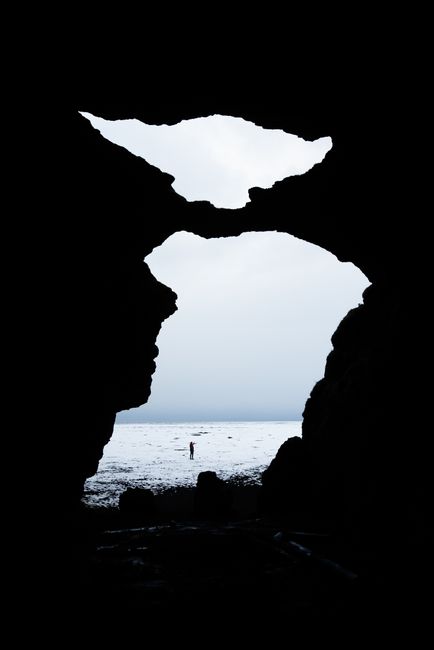 Silhouette view from a cave entrance looking out to the ocean, with a lone figure in the distance.