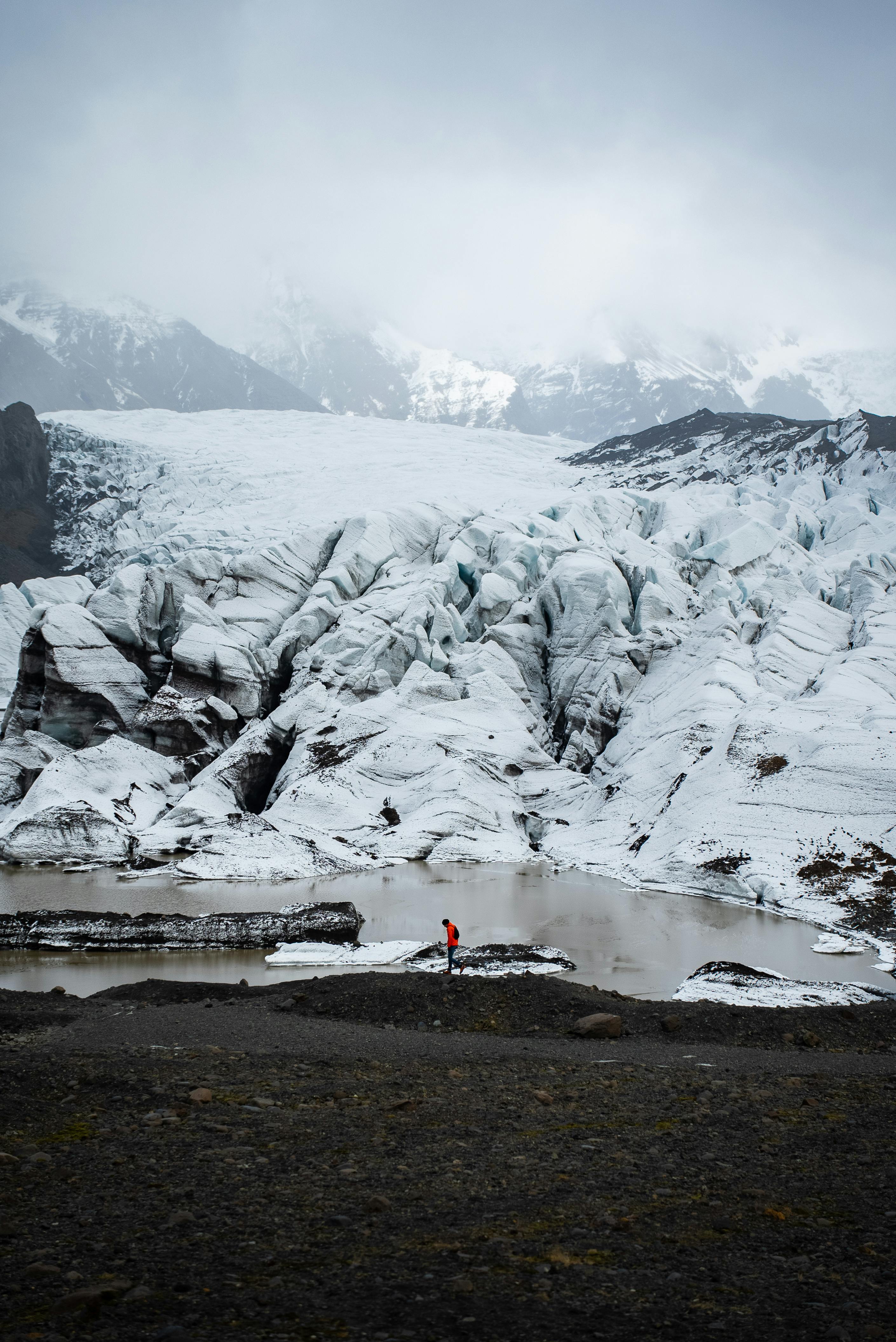 A scenic winter view of a person in a red jacket near a vast icy glacier.