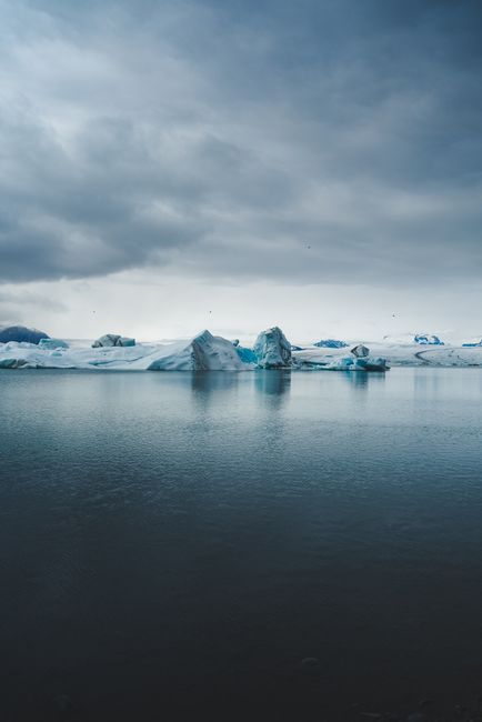 View of serene icebergs under a dramatic cloudy sky, embodying a sense of cold tranquility.