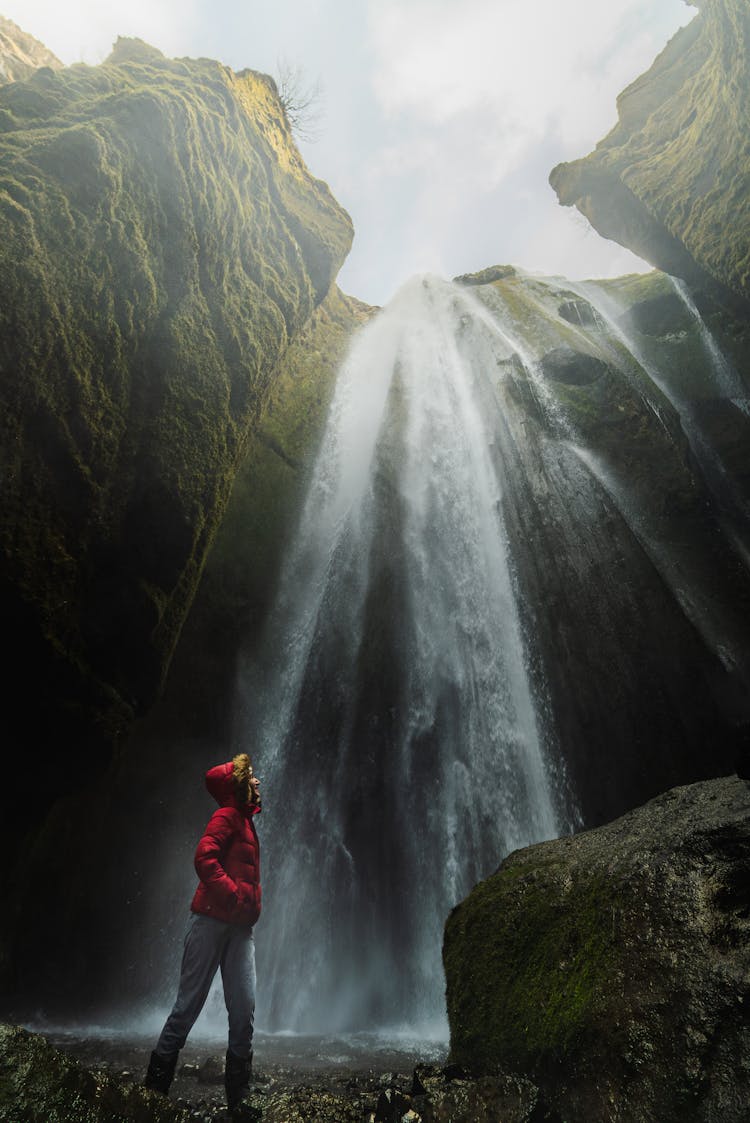 Hiker Standing Under Waterfall In Fjadrargljufur Canyon