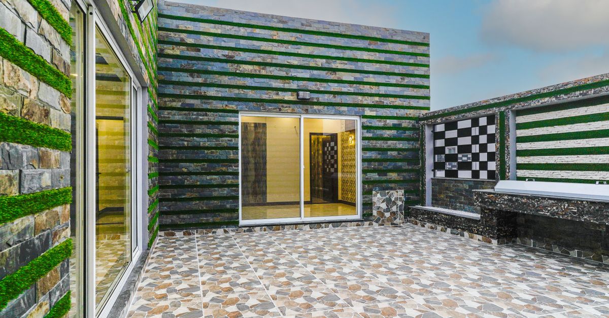 A contemporary outdoor patio featuring geometric tiles and green wall accents under a clear sky.