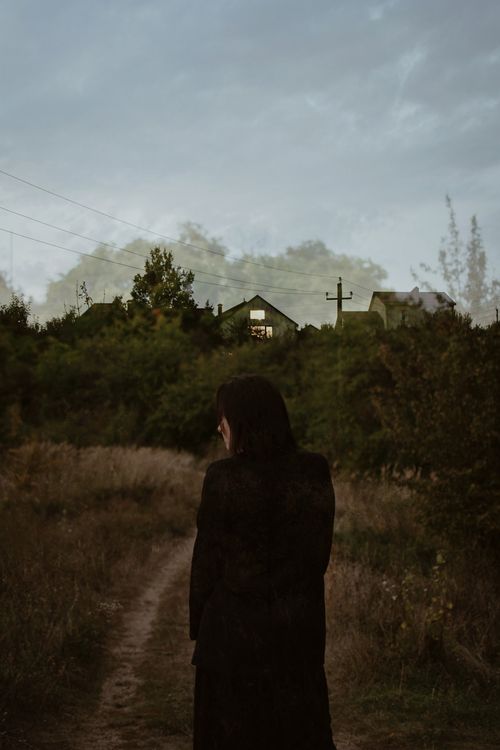 Free A solitary silhouette of a woman walking on a countryside path during twilight, surrounded by nature. Stock Photo