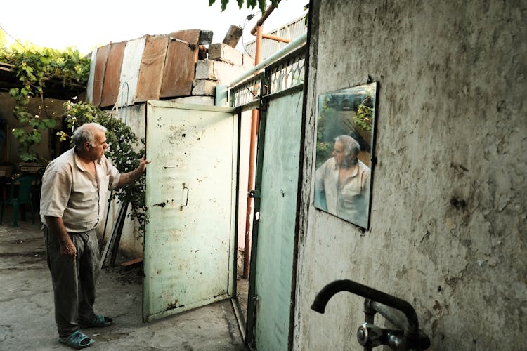 Elderly Man Standing And Holding Open Door