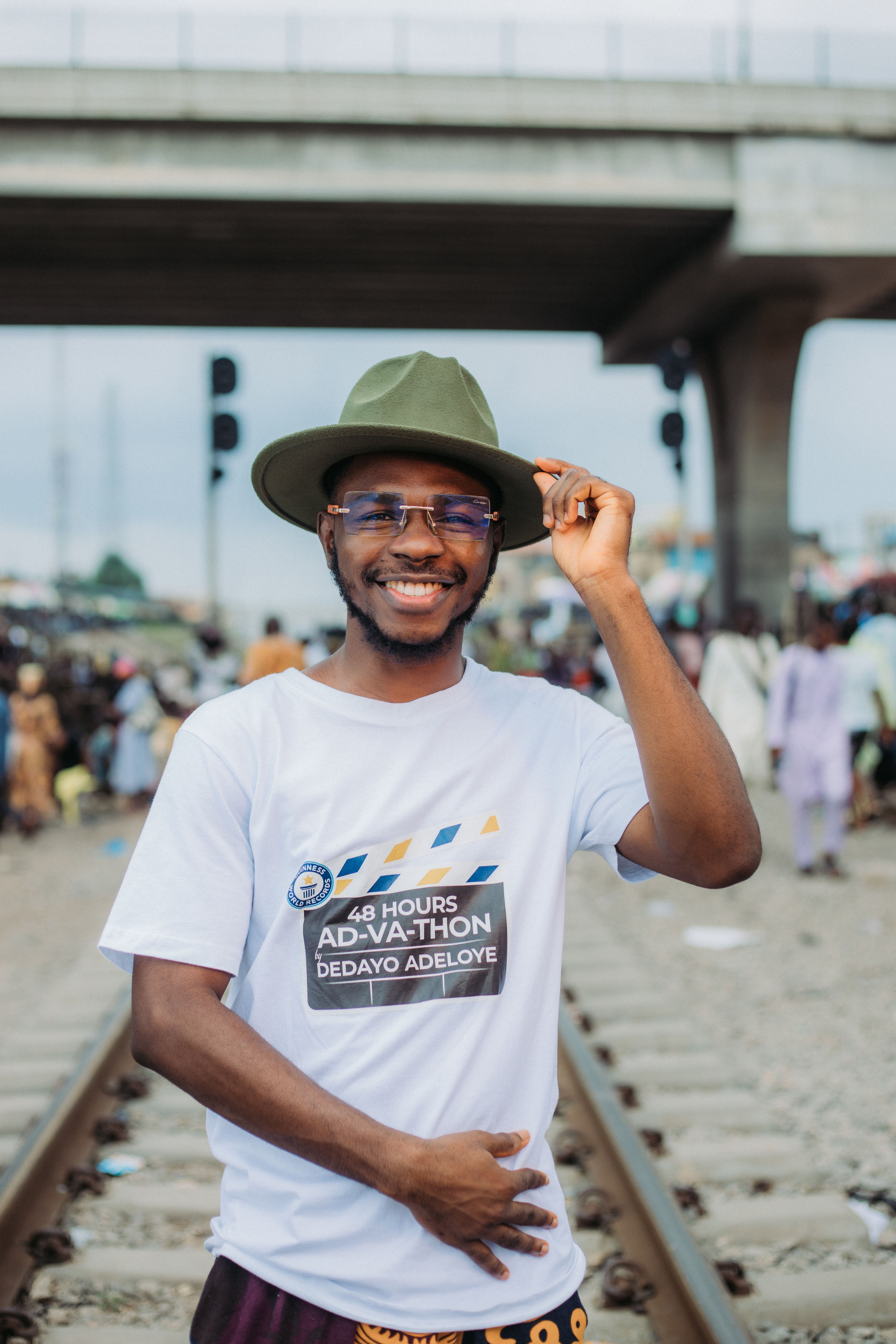 Cheerful man in a green hat stands by railway tracks, smiling at the camera.