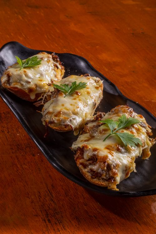 Free Three slices of cheesy beef toasts garnished with parsley on a black plate, ideal for a comfort food shot. Stock Photo
