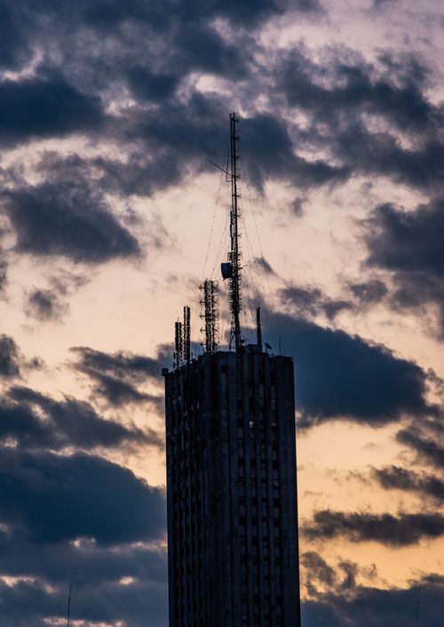 Free A towering silhouette of a modern building with antennas against a dramatic cloudy twilight sky. Stock Photo