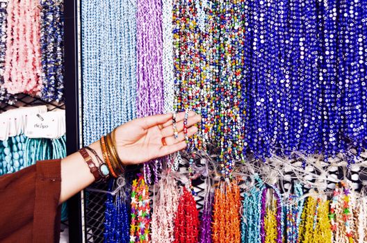A vibrant collection of beads on display with a hand selecting a strand in a shop.