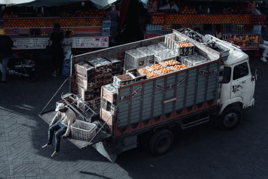 A truck loaded with crates of oranges parked at an urban market scene during daytime.
