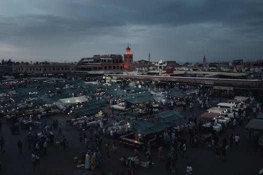 A vibrant night market in Marrakech bustling with people under a dusky sky.