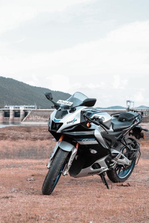 Free A sleek motorcycle parked in a serene rural setting with a dam and mountains in the background. Stock Photo