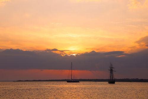 Free Beautiful sunset over the sea with silhouetted sailing vessels, creating a peaceful and scenic view. Stock Photo