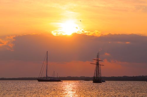 Free Beautiful sunset over the ocean with sailboats silhouetted against the warm sky. Stock Photo