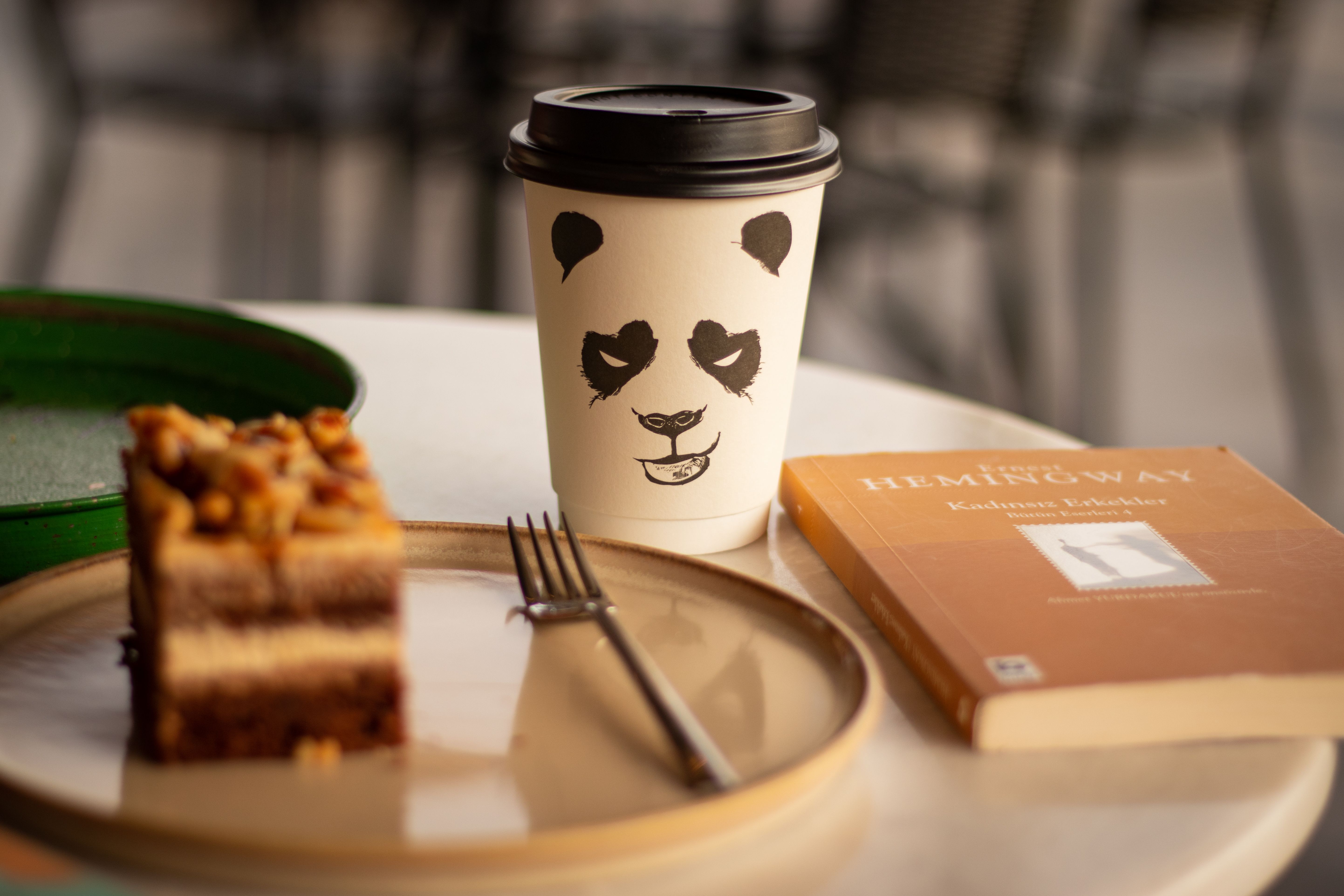 Elegant café scene featuring a coffee cup, cake slice, and a book on a table.
