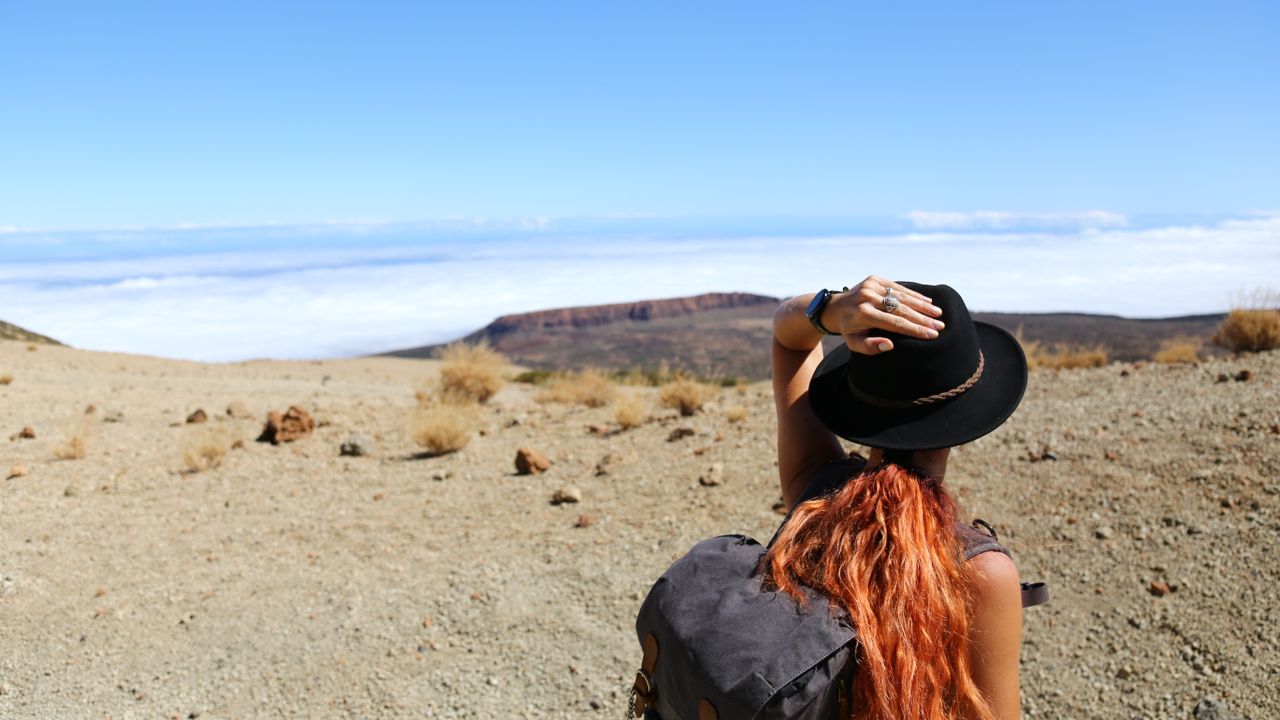 Woman with backpack standing in a landscape looking towards distant mountains.