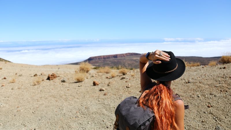 Woman with backpack standing in a landscape looking towards distant mountains.