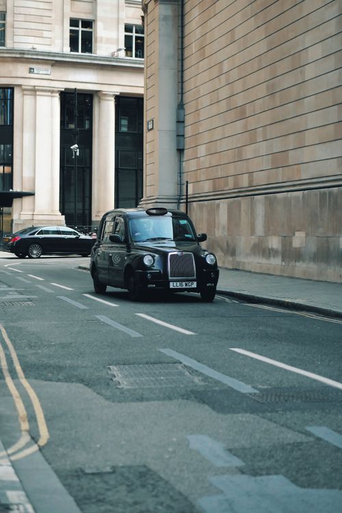Free Classic black taxi driving down a historic London street, showcasing urban life. Stock Photo