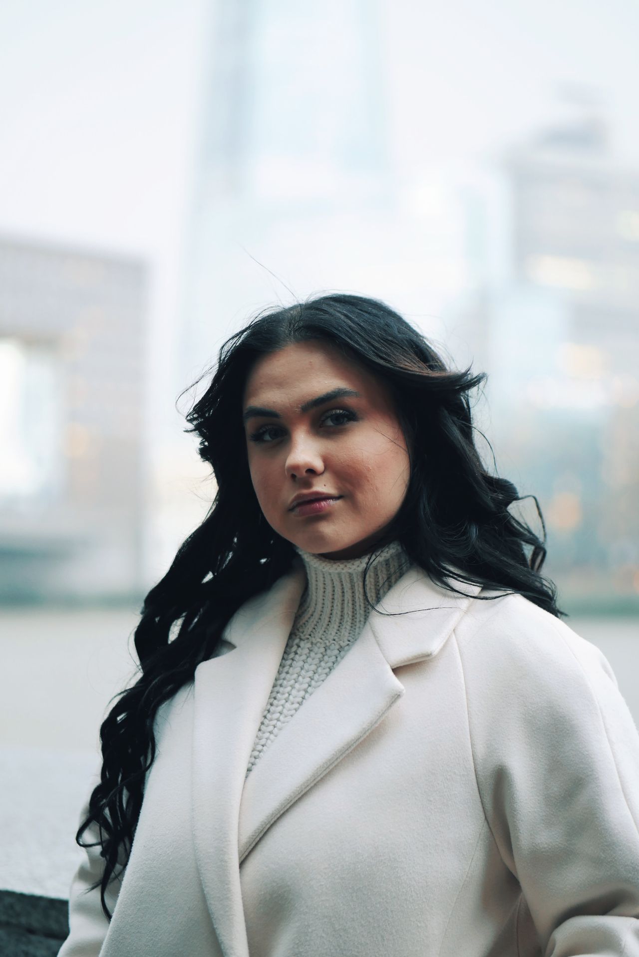 Woman in a white winter coat worn over a cream turtleneck knit sweater