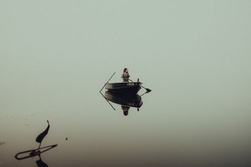 Free A lone woman in a boat on a foggy lake reflecting an overcast sky. Stock Photo