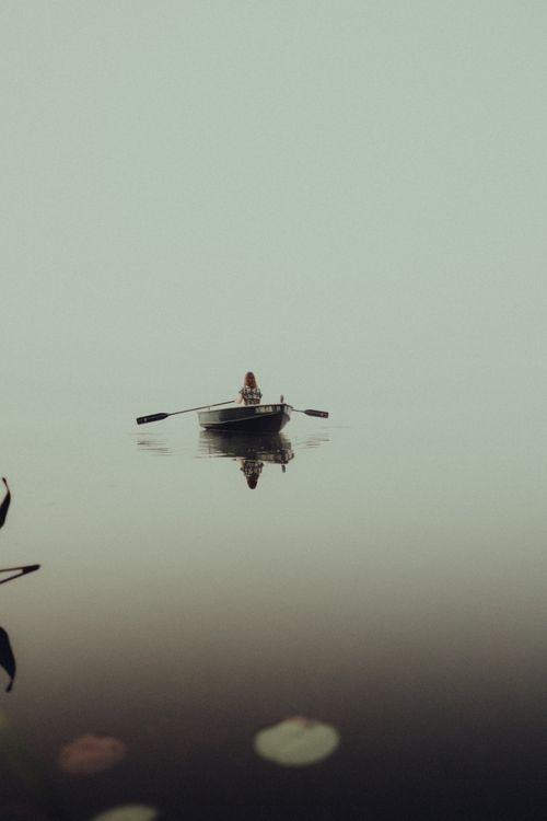 Free An serene image of a woman rowing a boat on a foggy lake, capturing calmness and reflection. Stock Photo