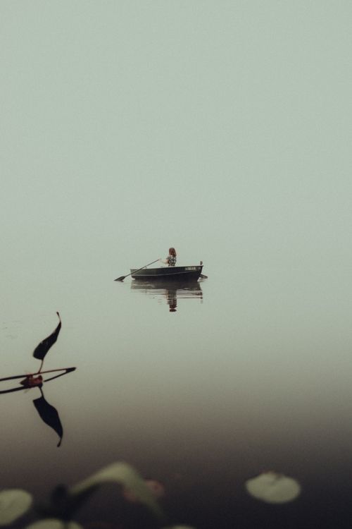 Free A serene scene of a solitary rowboat on a calm lake with minimalistic reflections. Stock Photo
