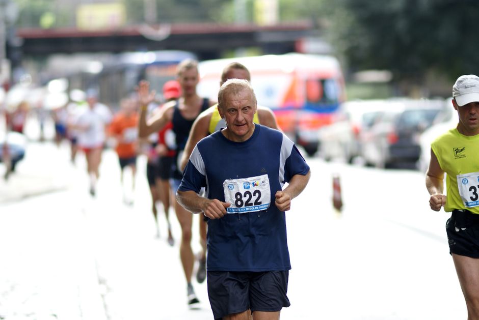 Senior participant leading a city marathon surrounded by other runners, showcasing determination and fitness.
