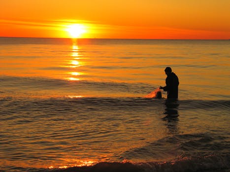 Silhouette of a man fishing at sunset on a calm sea, creating a peaceful and serene scene.