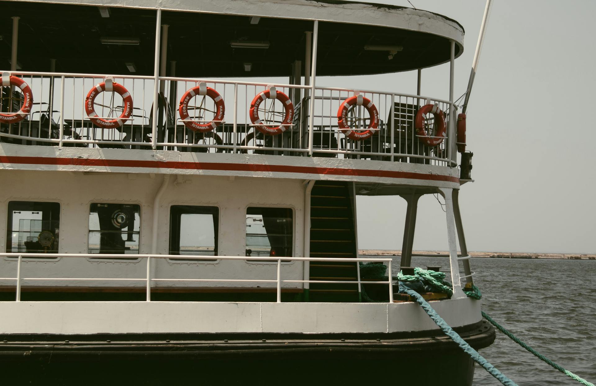 Close-up of a vintage ferry boat with lifebuoys on calm sea, featuring nautical details and serene waters.