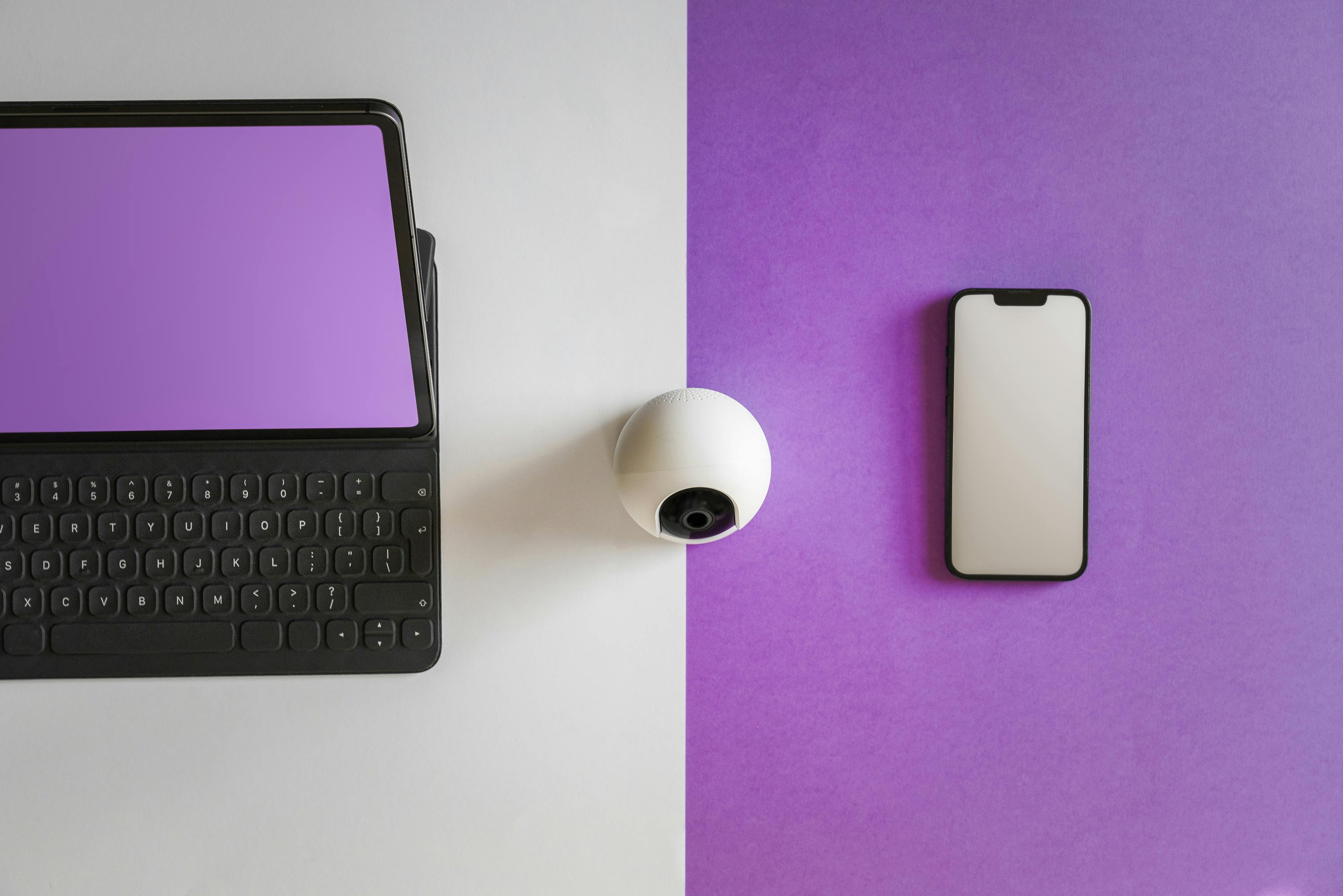 Minimalist setup featuring a tablet, smartphone, and spherical webcam on a split colored background.