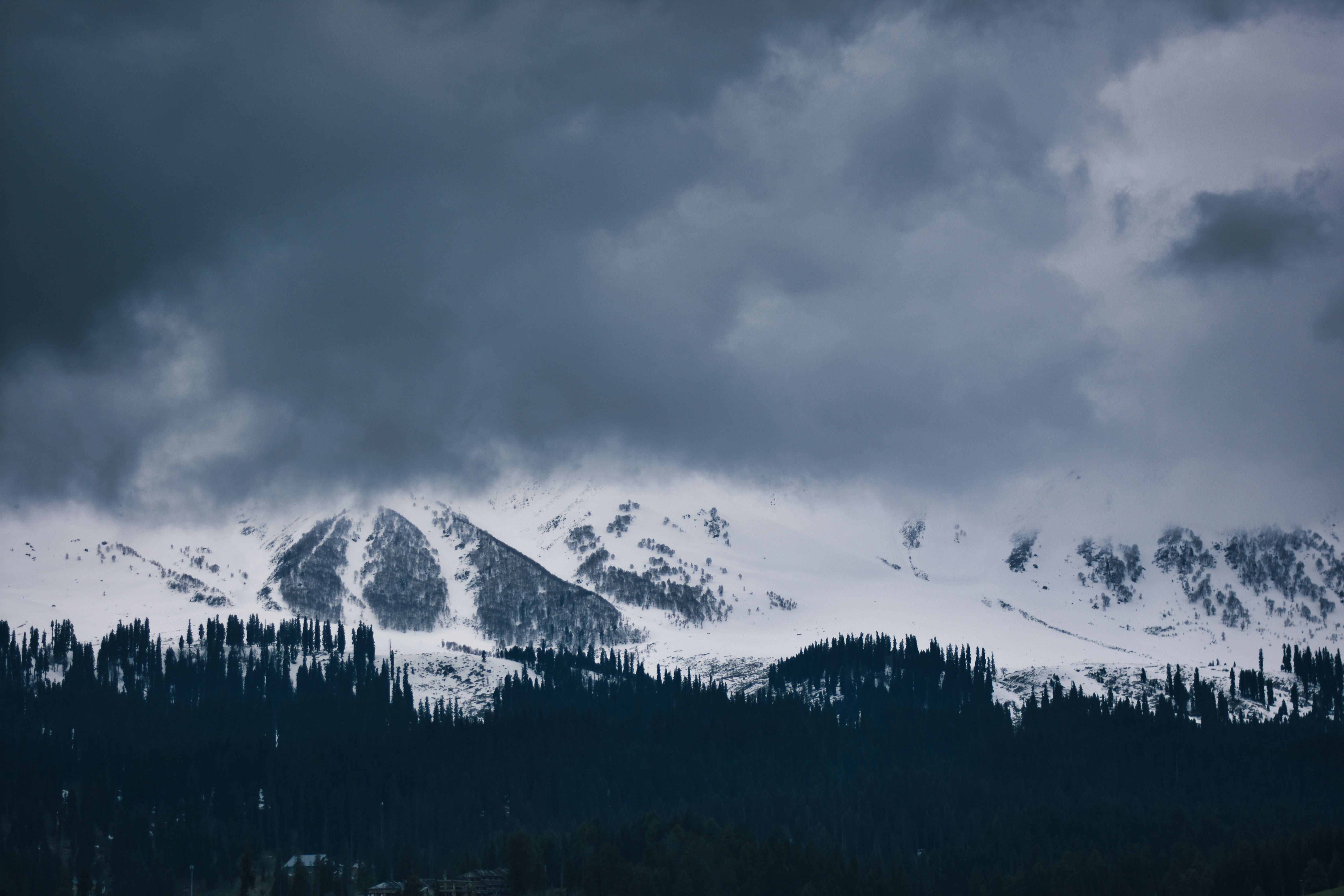 Representative photograph of snowy mountains under storm clouds in India; not an image of Alaska or the October 2026 storm