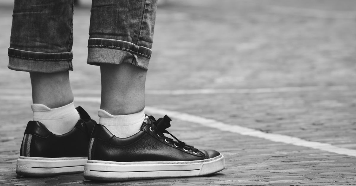 A close-up black and white image of casual sneakers standing on cobblestone pavement.