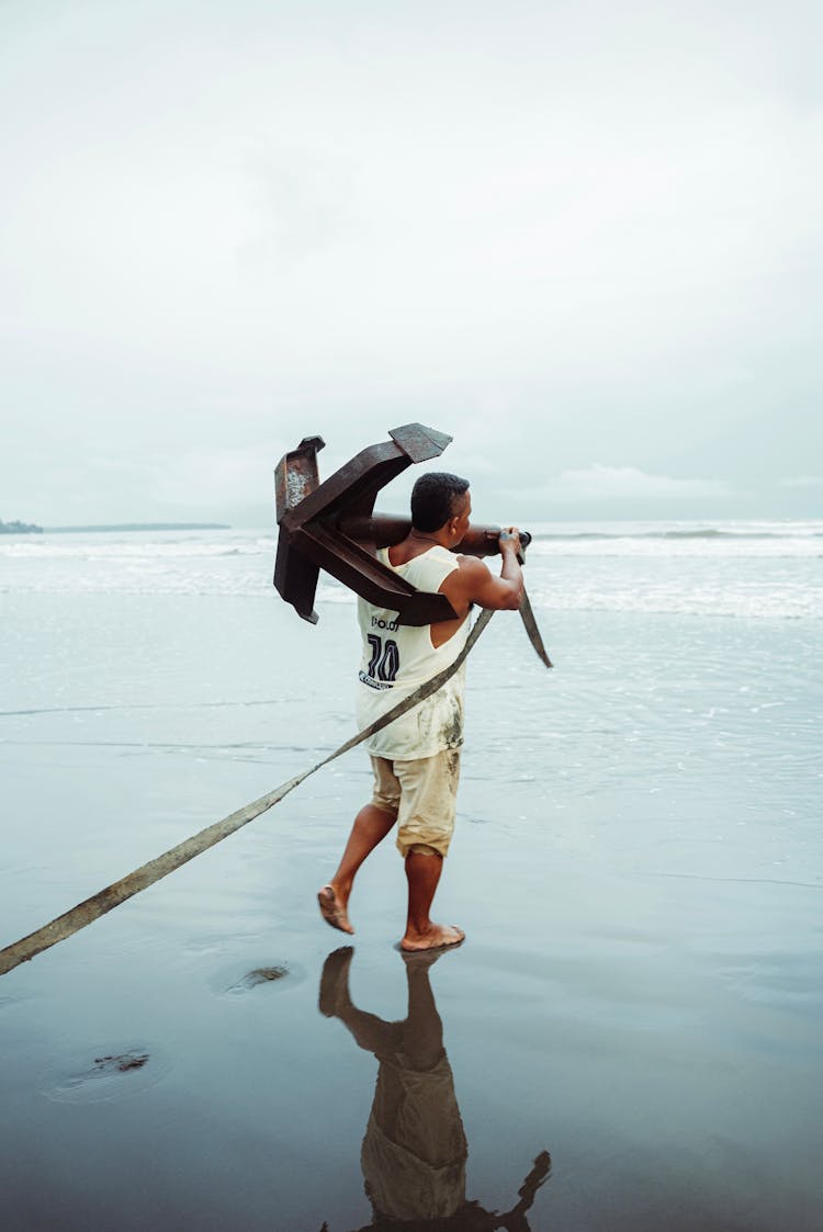 Man Carrying Anchor On Sea Shore