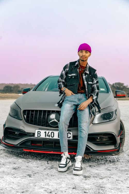 Free A fashionable man in casual attire poses confidently with a Mercedes-Benz sports car outdoors. Stock Photo