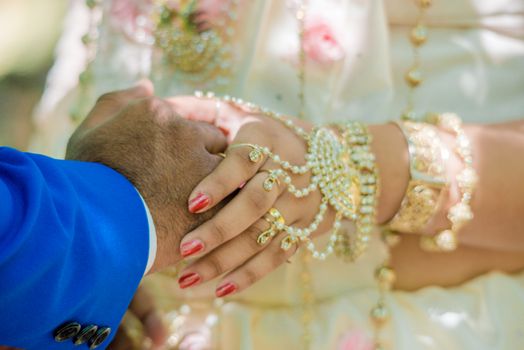 A close-up of a couple's hands adorned with traditional Indian jewelry during a wedding.