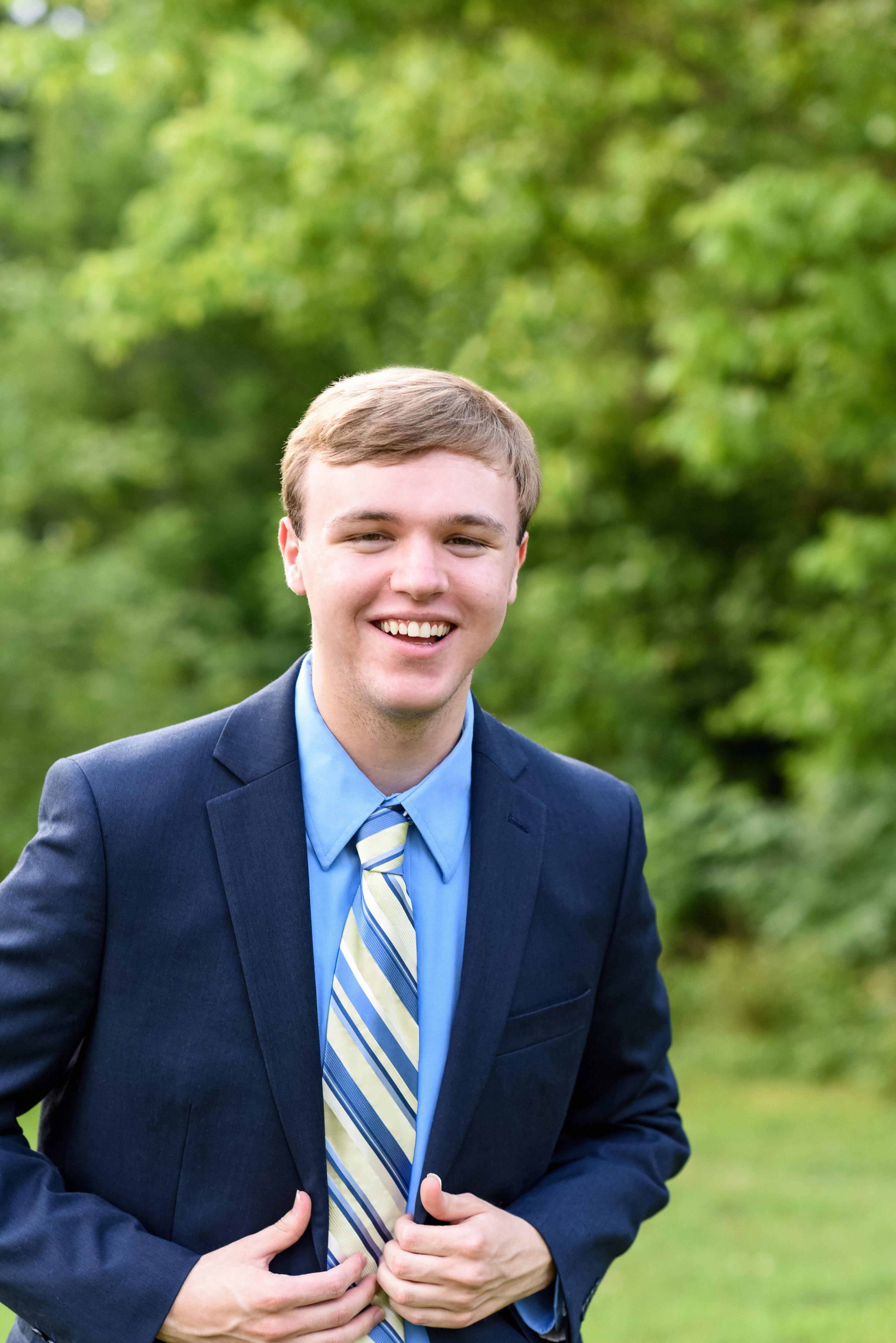 Young man in a blue suit smiling confidently against a natural background.