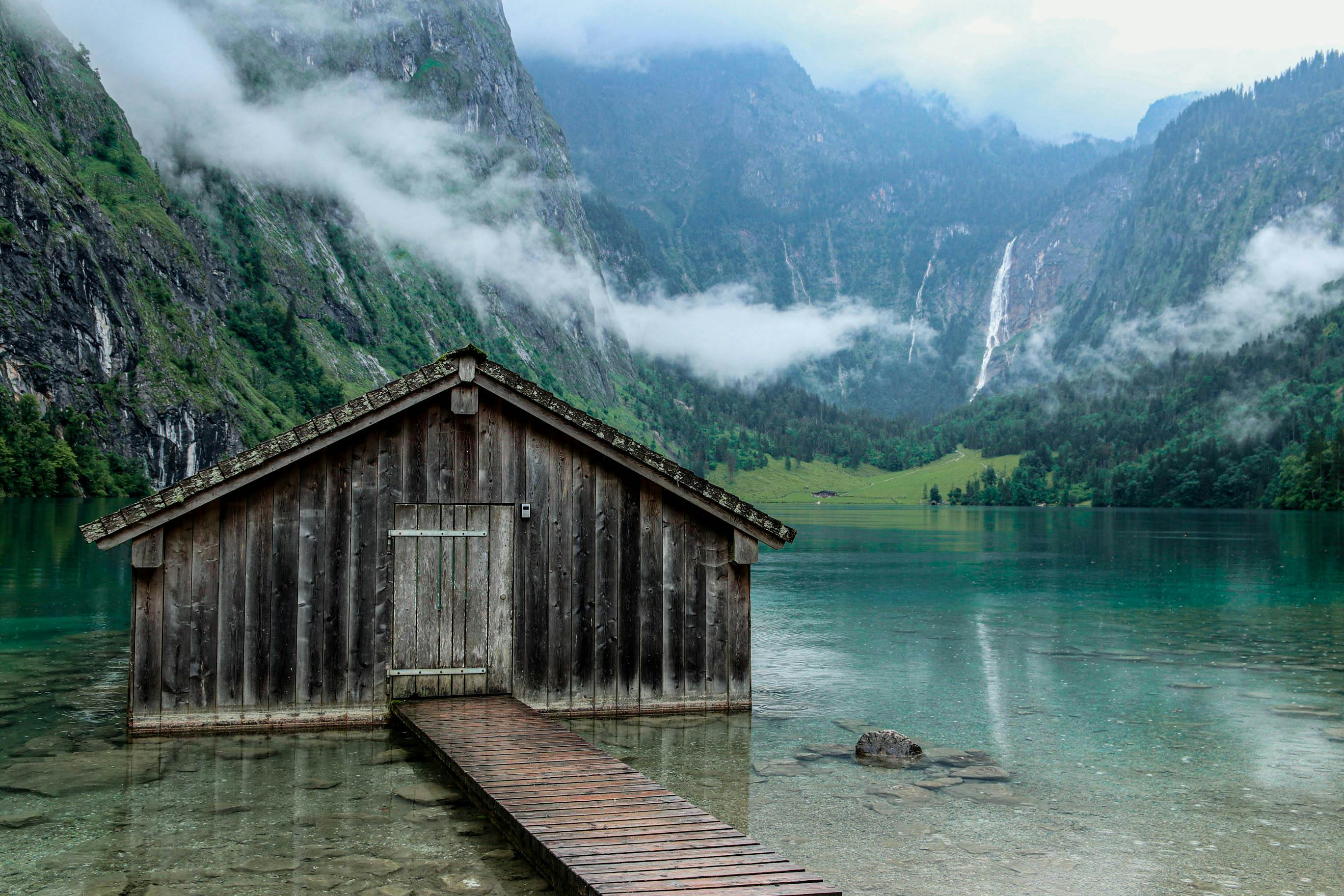 Tranquil wooden cabin at Königsee with misty mountains and lush greenery.