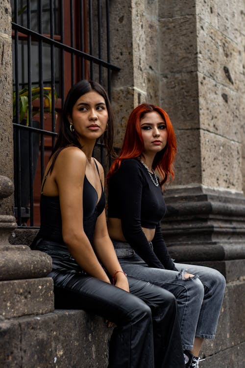 Two Female Models Sitting on a Wall
